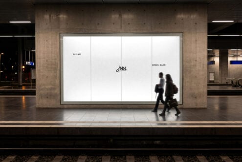 Large backlit billboard in modern subway station with blurred commuters walking past