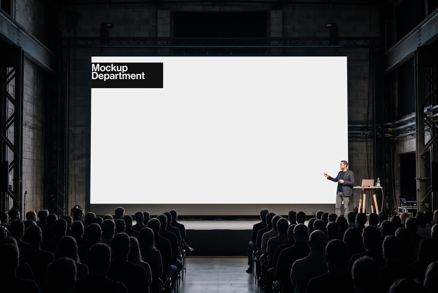 Speaker presenting to packed audience with giant projection screen in industrial venue