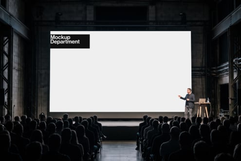 Speaker presenting to packed audience with giant projection screen in industrial venue