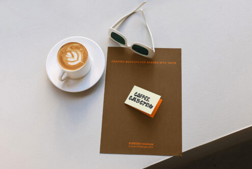 Flat lay showing brown magazine with sticky note, latte with latte art, white sunglasses on gray background