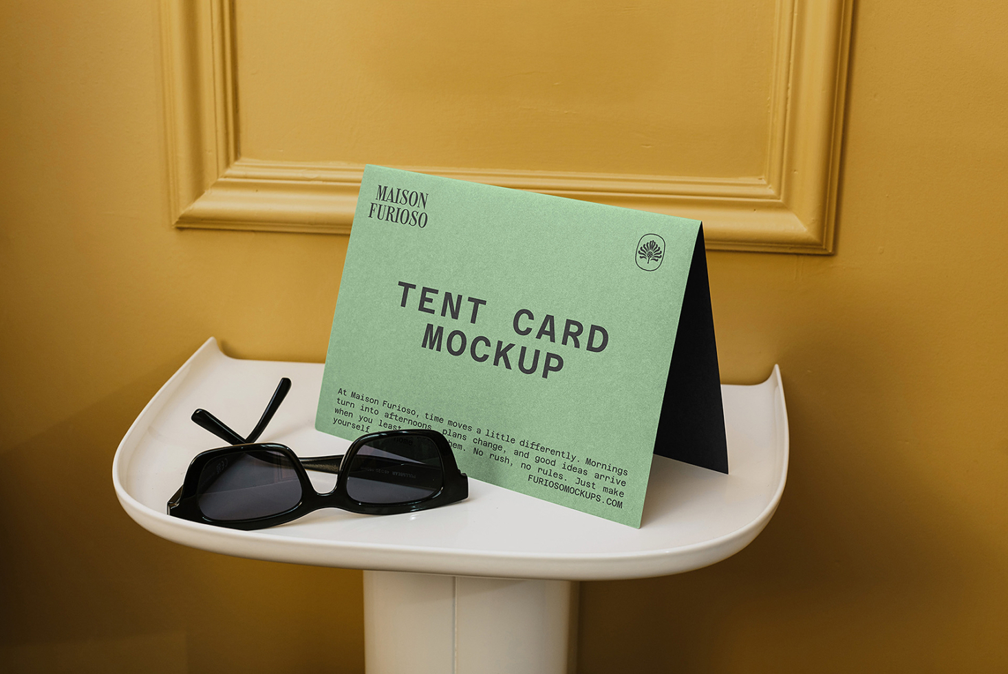Mint tent card mockup displayed on white pedestal table with black sunglasses against gold wall