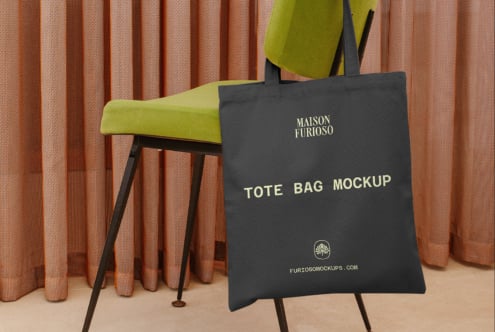 Black tote bag mockup on easel with lime green chair, terracotta curtains backdrop