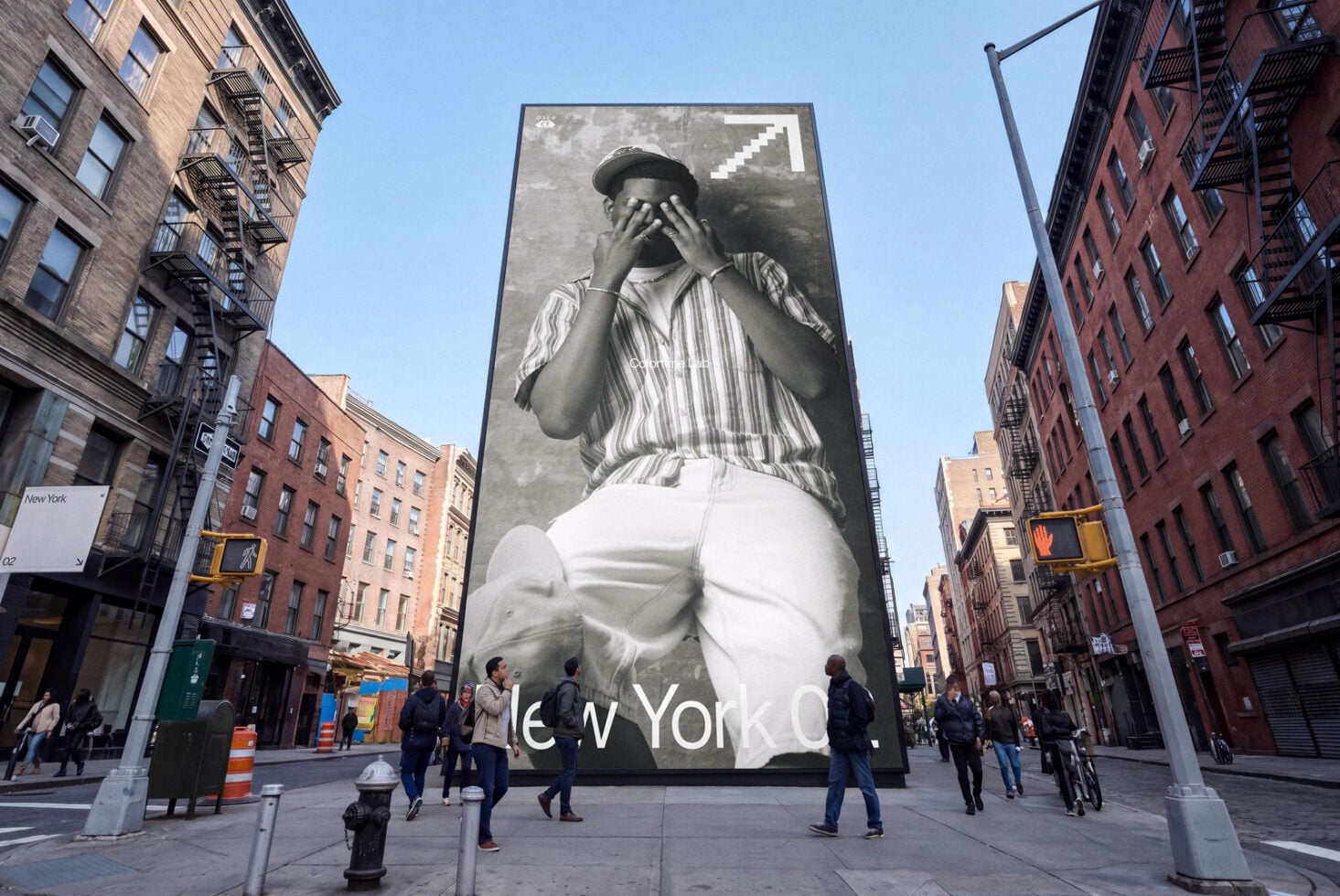 Massive black white billboard of man in hat covering face, NYC street below with brick buildings