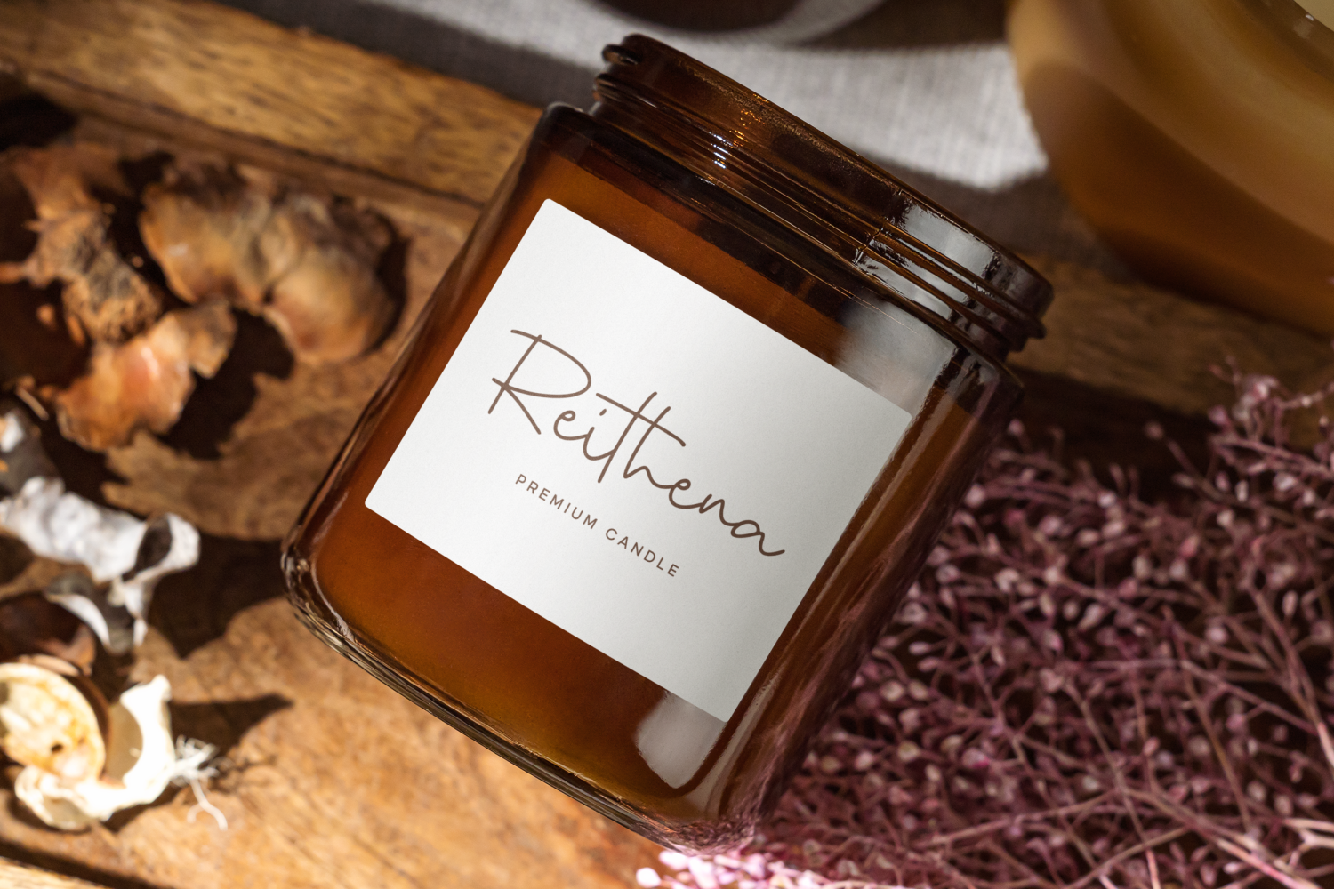 Amber glass jar with Rethea premium candle label surrounded by dried flowers on wooden surface