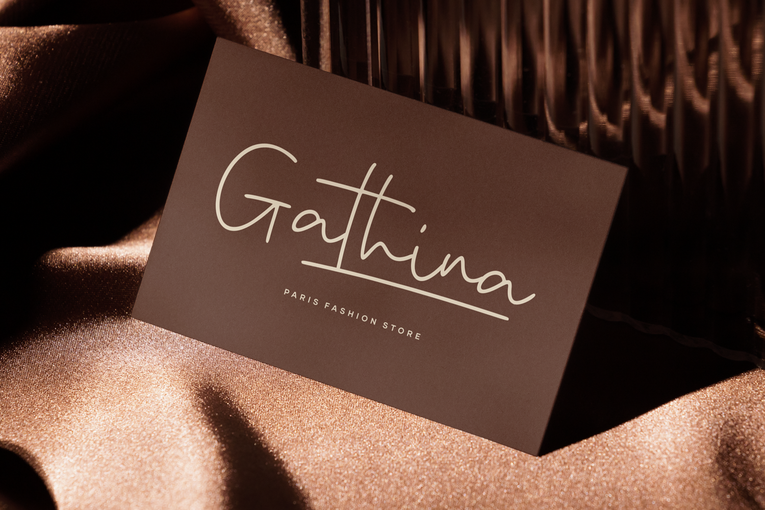 Luxury business card mockup with handwritten serif logo on brown cardstock, styled on bronze fabric with dramatic lighting