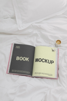 Open magazine spread on white bedding with coffee cup, showing black left page with yellow text, cream right page with black text