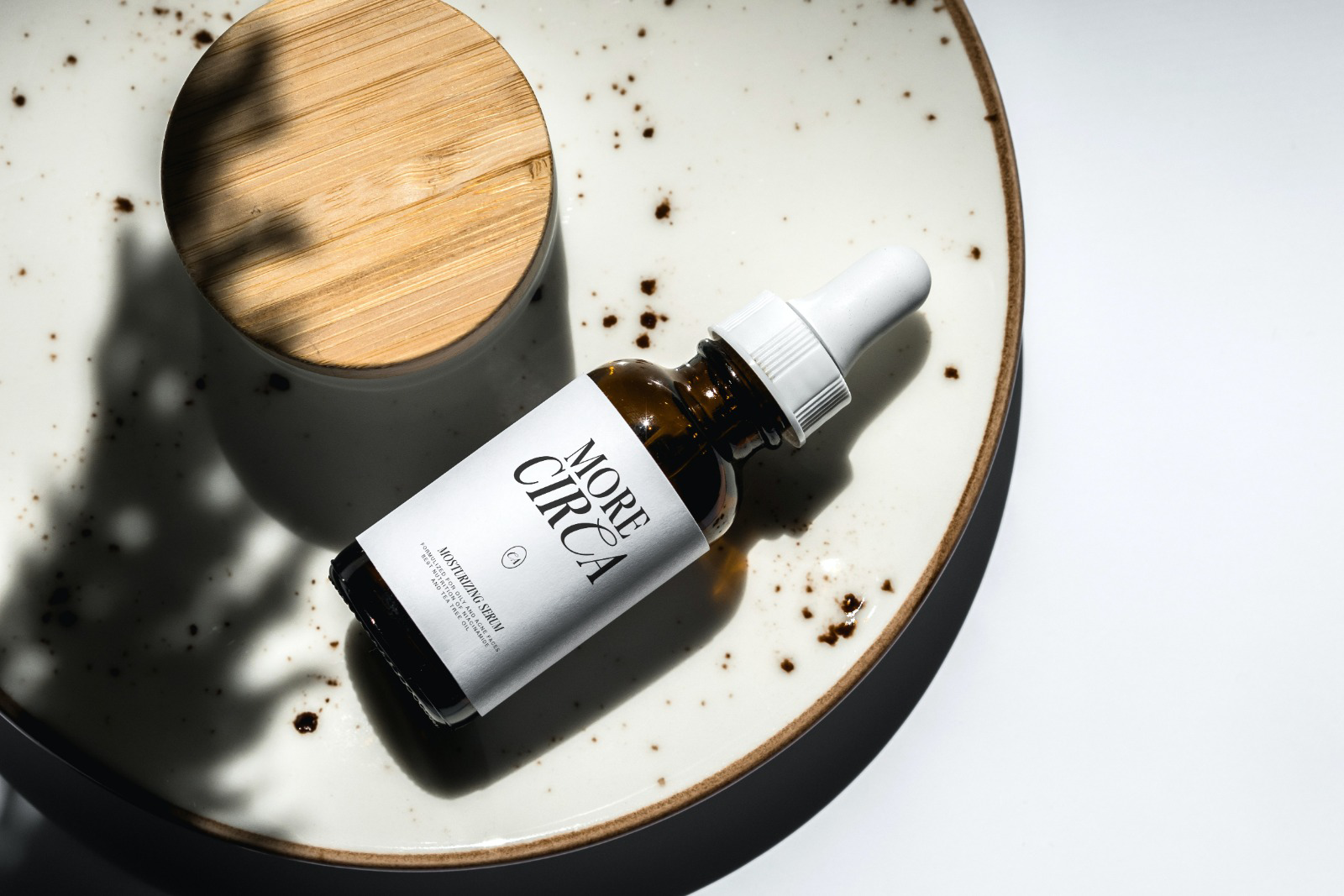 Skincare serum bottle with white label next to wooden bowl, coffee grounds scattered on ceramic dish