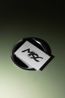 Business card mockup with bold black logo on white card resting in sleek black bowl, sage green background