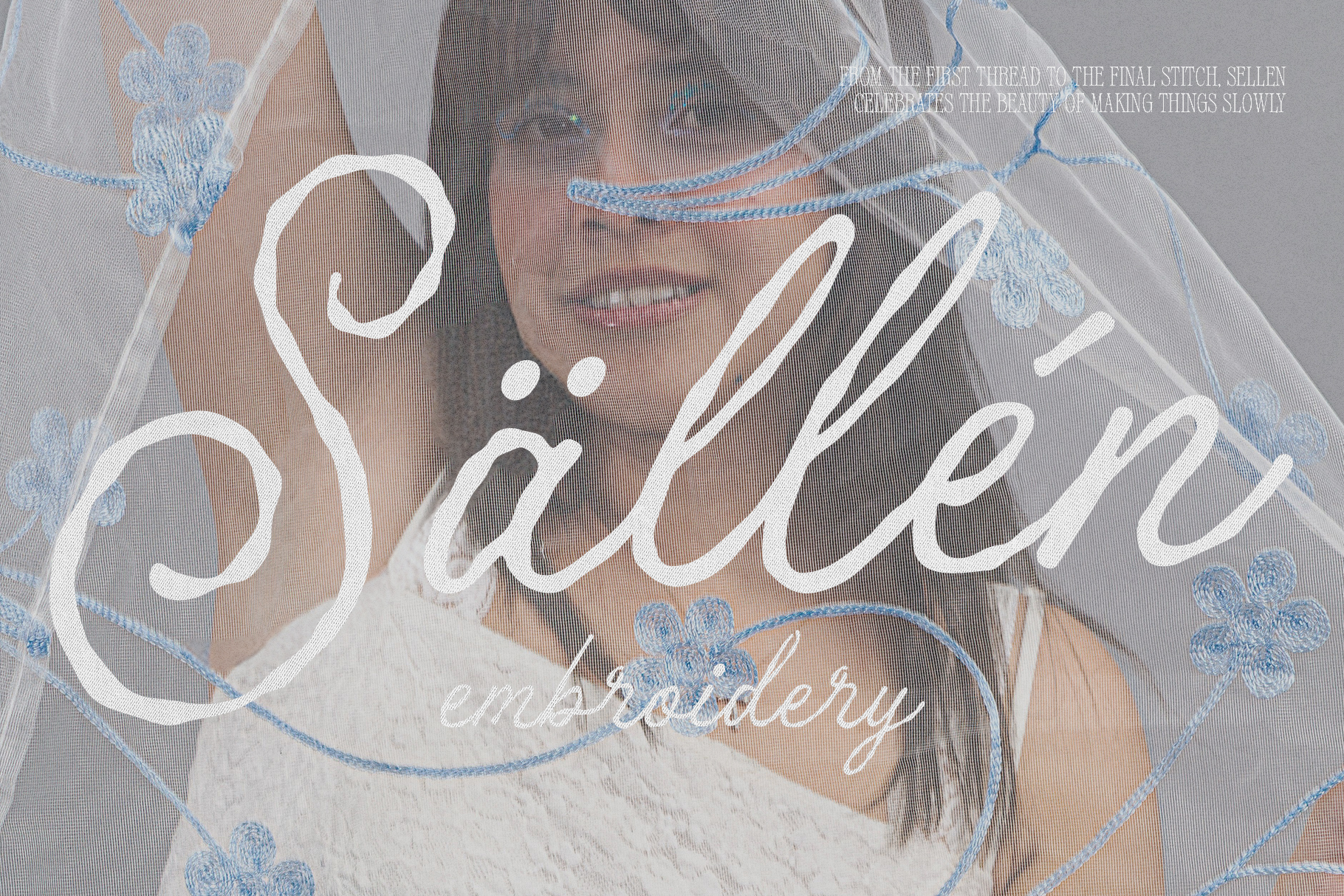 Embroidered textile with flowing script lettering over delicate floral stitching in blue tones
