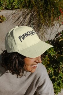 Cream baseball cap with FURIOSO text on model in sunny garden setting with ivy