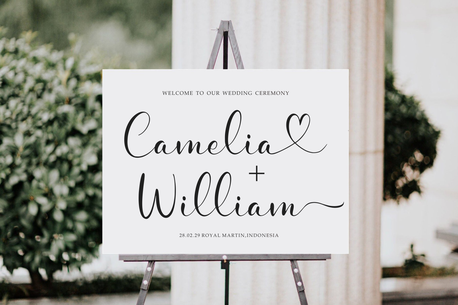 Elegant wedding ceremony sign on easel with couple's names in flowing script, garden backdrop with white flowers