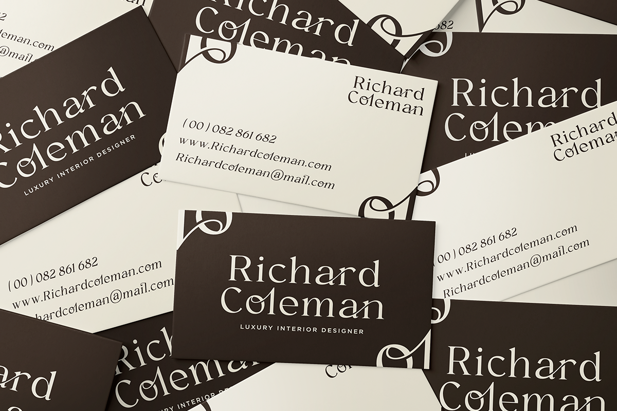 Business cards scattered showing luxury interior designer branding with cream, black, ornate details