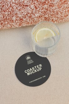 Round black coaster mockup with lemon water glass on textured beige surface