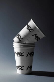 Stacked coffee cups with tilted lid showing edgy black logo branding on white paper cups