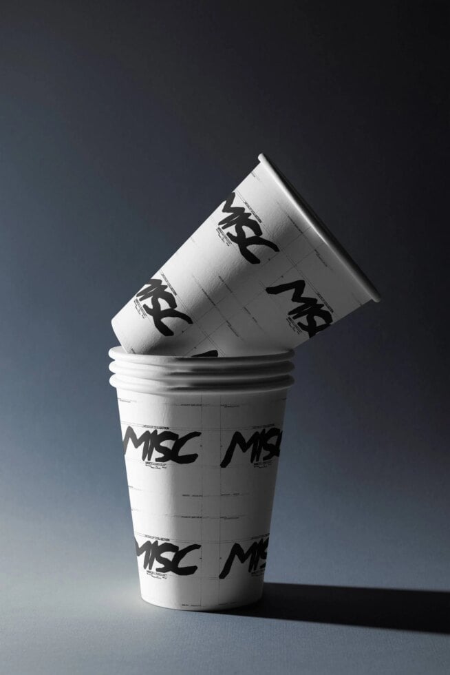 Stacked coffee cups with tilted lid showing edgy black logo branding on white paper cups