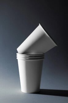 Stacked white paper cups with angled cone cup on top, minimal dark background