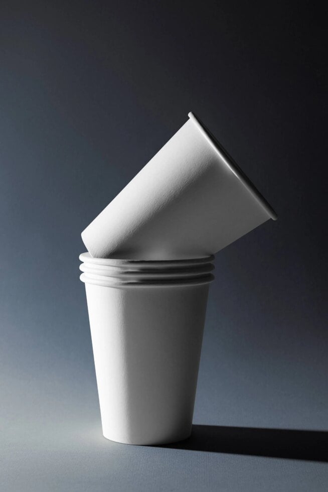 Stacked white paper cups with angled cone cup on top, minimal dark background
