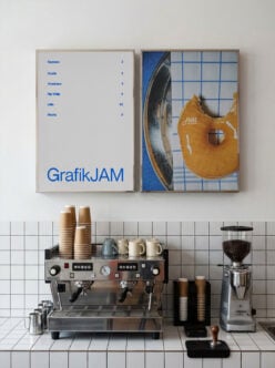 Cafe counter with espresso machine, grinder, stacked cups, framed GrafikJAM poster above white subway tile