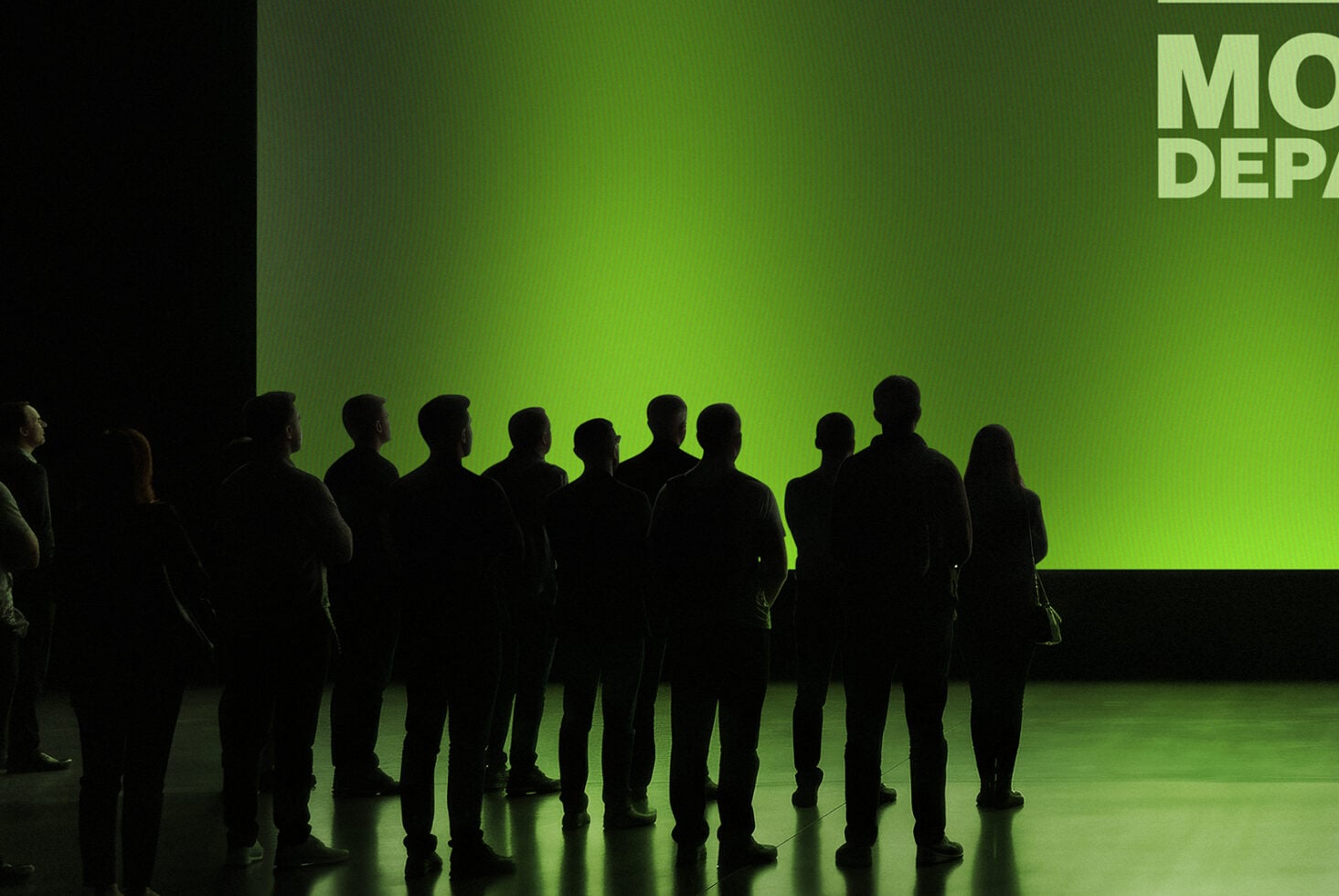 Silhouetted group of people standing in front of bright lime green screen display