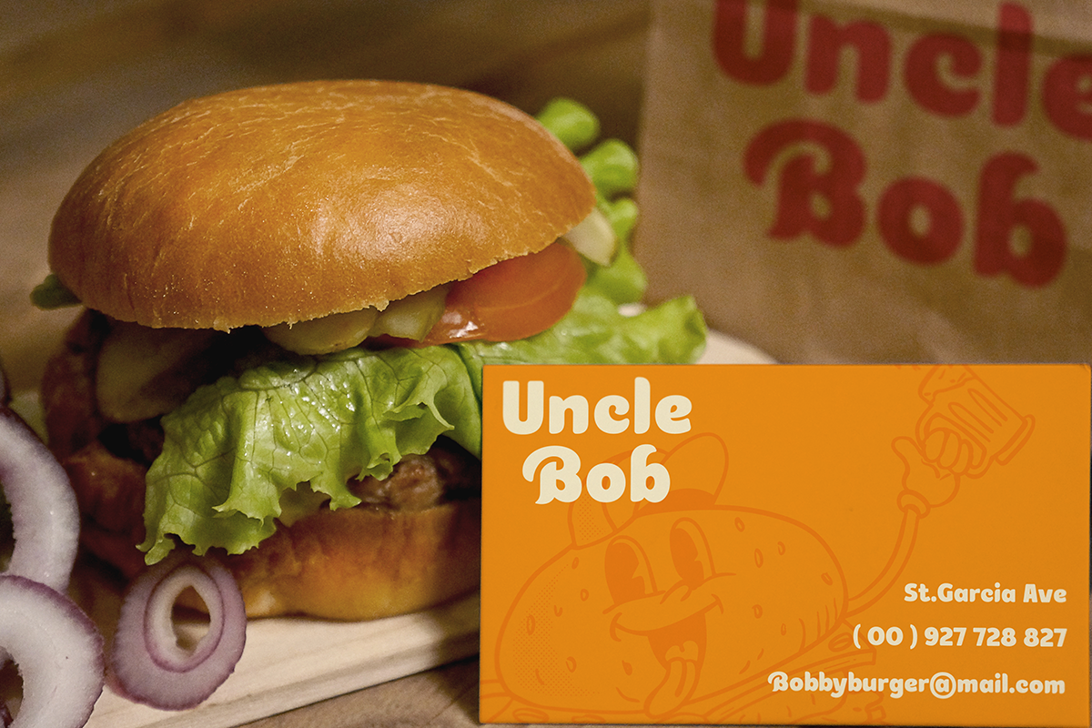 Juicy burger with lettuce, tomato, onions next to orange Uncle Bob business card mockup
