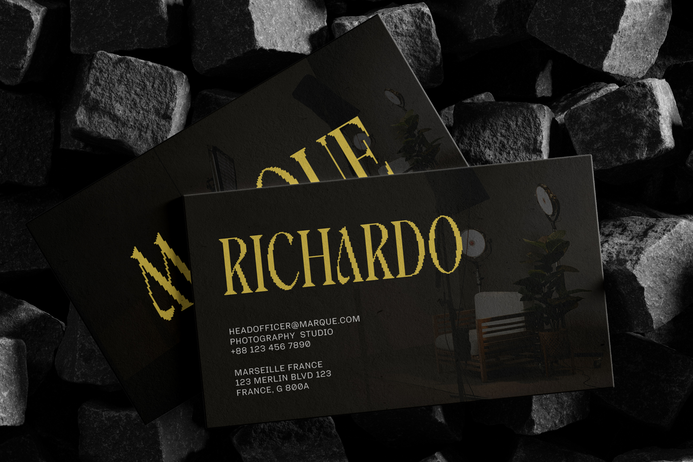 Black business cards with gold foil lettering scattered on textured stone background