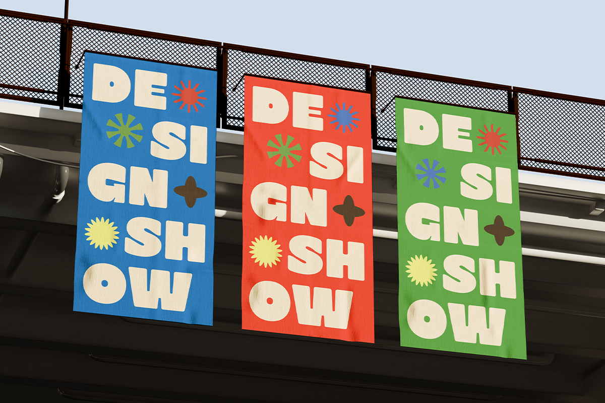 Retro design shop storefront with three colorful hanging signs in blue, red, green featuring bold cream lettering with playful geometric icons