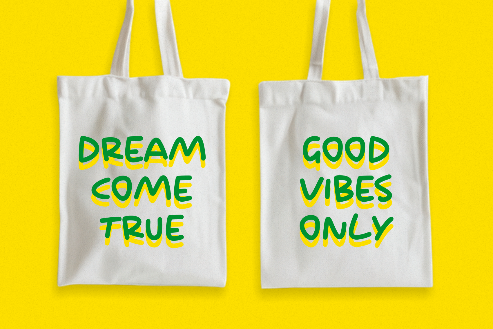 Two white canvas tote bags with green plus yellow text saying "Dream Come True" plus "Good Vibes Only" on bright yellow background