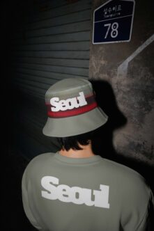 Person wearing Seoul bucket hat with matching sweatshirt in gritty urban setting