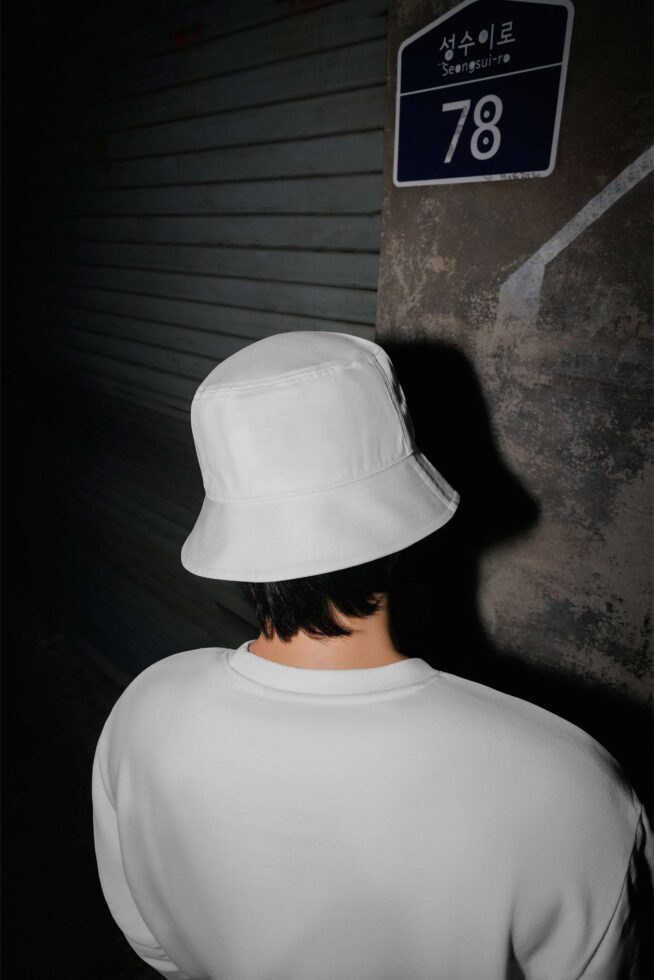 White bucket hat mockup on person wearing cream sweatshirt against grungy urban backdrop