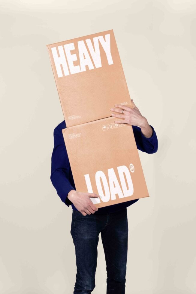 Person holding stacked cardboard boxes with "HEAVY LOAD" text, navy sleeve visible