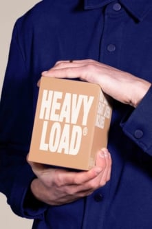 Person in navy shirt holding cardboard box with HEAVY LOAD printed in white text