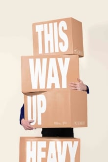 Person holding stacked cardboard boxes with bold white letters spelling out shipping message