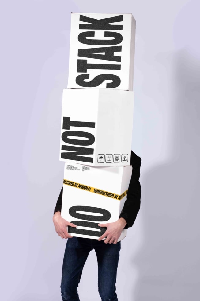 Stacked shipping boxes mockup with bold black typography, person holding them with head covered