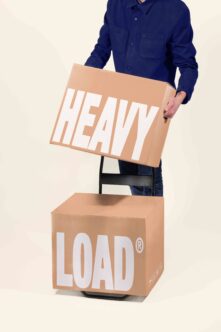 Person in navy shirt holding cardboard box with HEAVY text, stacked on LOAD box mockup