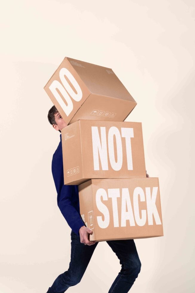 Guy struggling to carry three stacked cardboard boxes labeled "Do Not Stack"
