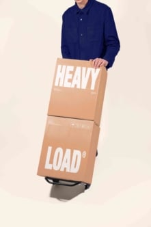 Guy in navy shirt holding stacked cardboard boxes labeled HEAVY LOAD with shipping icons