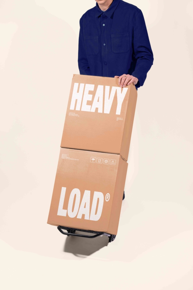 Guy in navy shirt holding stacked cardboard boxes labeled HEAVY LOAD with shipping icons