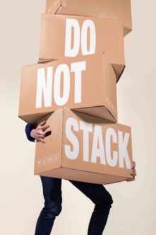 Stacked cardboard boxes with "DO NOT STACK" text, person carrying them in jeans