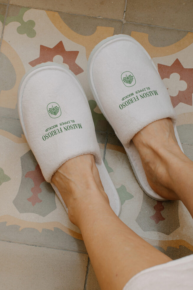 Feet in white spa slippers with green logo on colorful tile floor, overhead shot