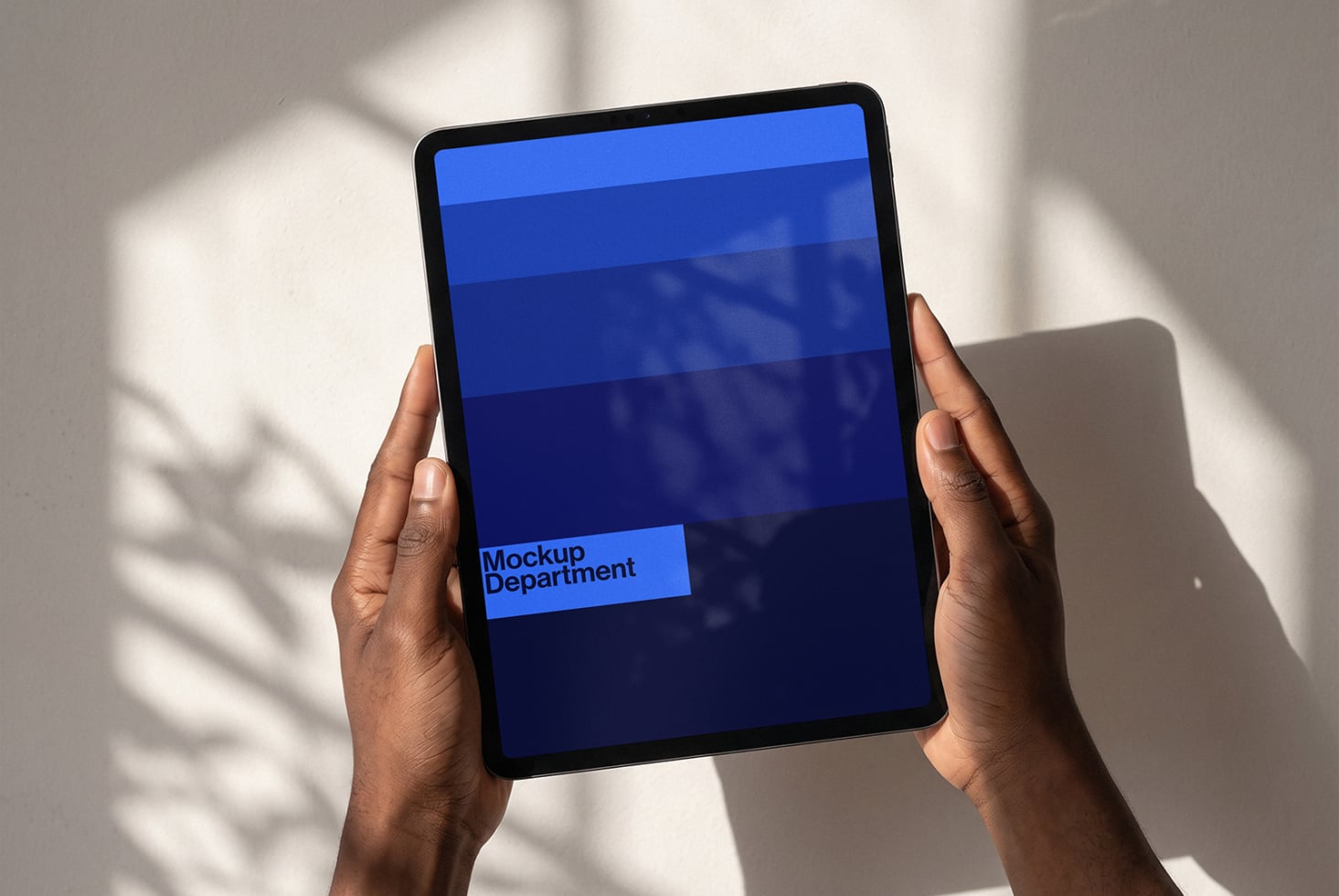 Hands holding tablet with blue gradient screen showing Mockup Department branding in natural light