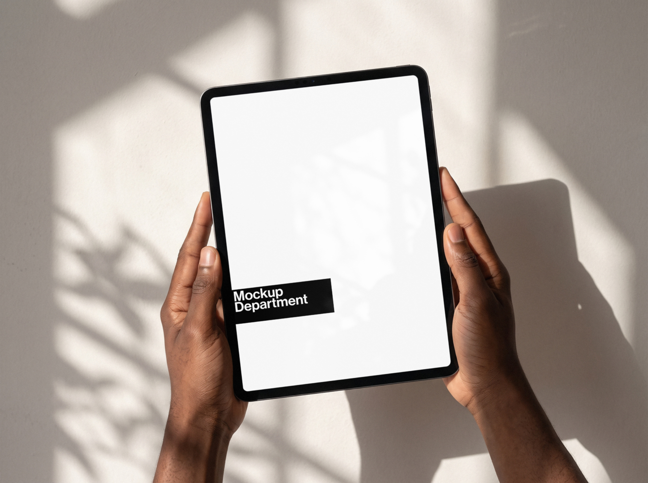 Hands holding tablet with Mockup Department branding on screen with natural shadow overlay