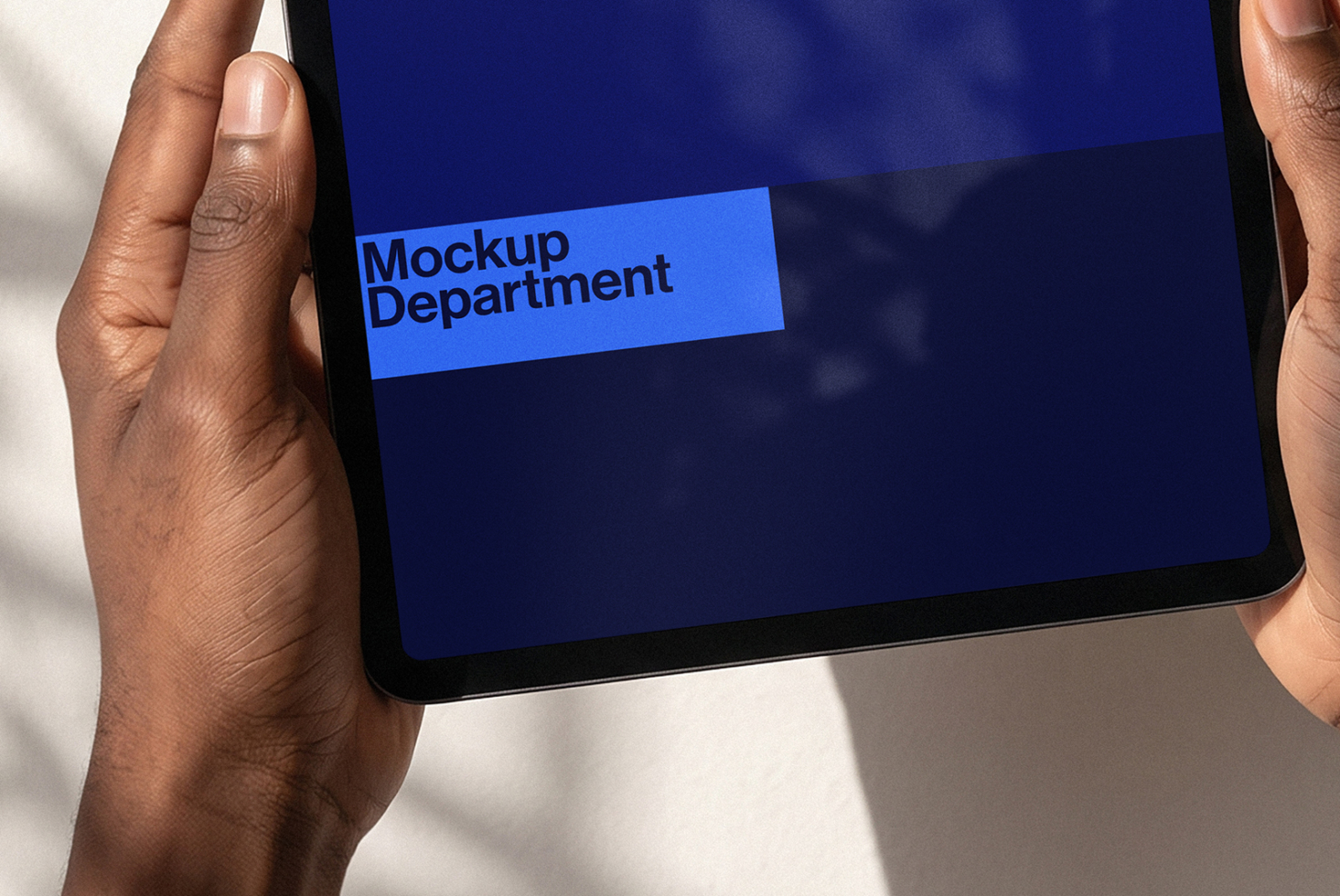 Hands holding tablet showing bright blue label with "Mockup Department" text on dark screen