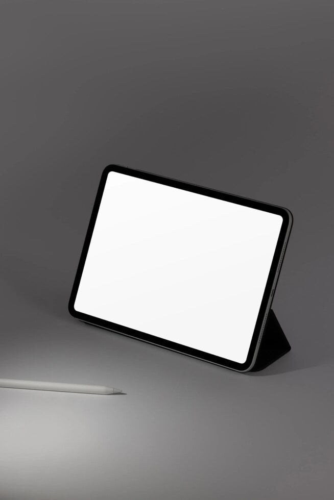 Tablet mockup with black case standing on gray surface next to stylus pen