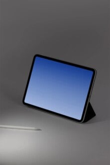 Black tablet in landscape mode with blue screen, sitting on gray surface next to stylus
