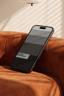 iPhone mockup resting on rust-colored velvet couch with natural light casting shadows