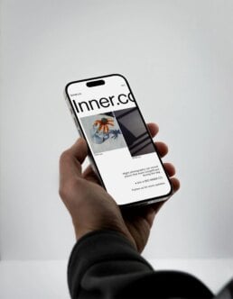 Hand holding iPhone displaying Inner.co website with minimalist layout, orange botanical imagery, dark photography