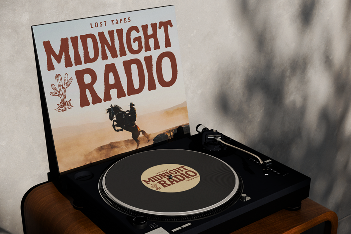 Vinyl record player with Midnight Radio album cover propped up behind it on wooden surface