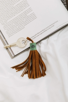 Leather tassel keychain with sage green tag sitting on open book with brass key