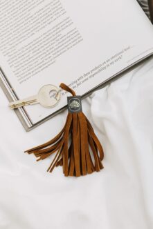 Leather tassel keychain with black tag sitting on open book next to brass key ring