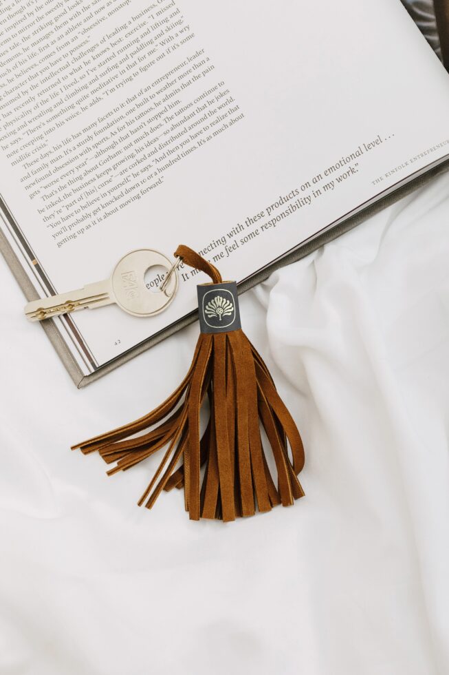 Leather tassel keychain with black tag sitting on open book next to brass key ring